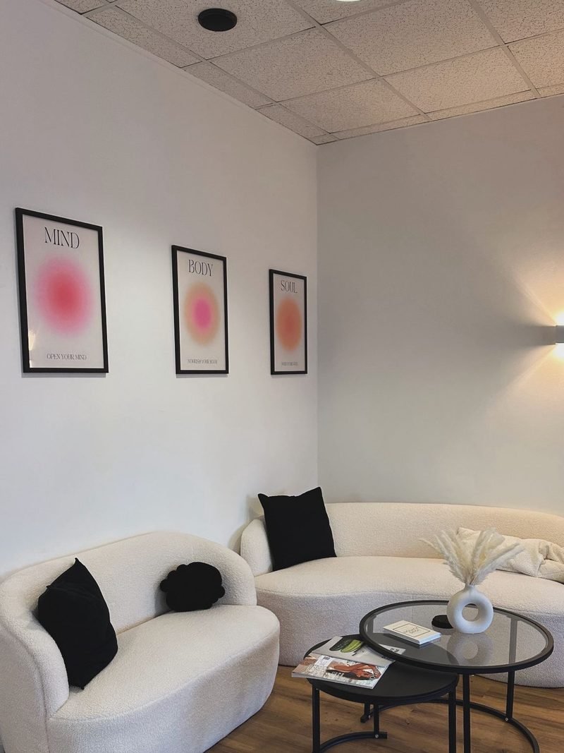 Lounge-Bereich mit wei&szlig;en Boucl&eacute;-Sofas, Marmortischen und drei gerahmten Mind-Body-Soul-Postern